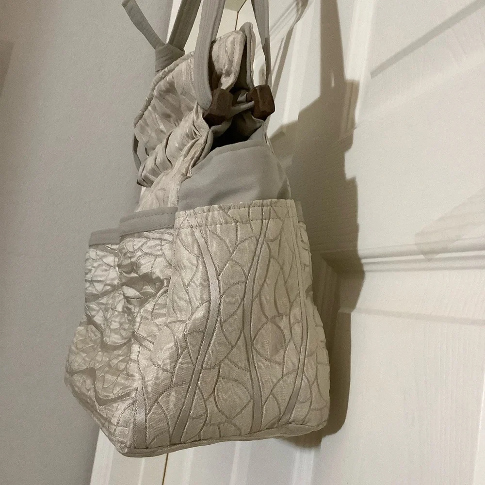 FABRIC SHOULDER BAG WITH OUTSIDE SURROUNDING POCKETS IN A CREAM AND TAUPE COLOR.